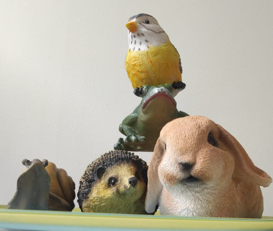 Des statues de jardin en résine. De gauche à droite : un escargot, un hérisson, un lapin. Une grenouille est posée sur le hérisson et le lapin. Un oiseau est posé sur la grenouille.